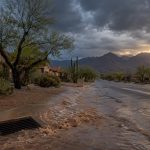 Flooded street and storm drain beside desert homes under monsoon storm clouds