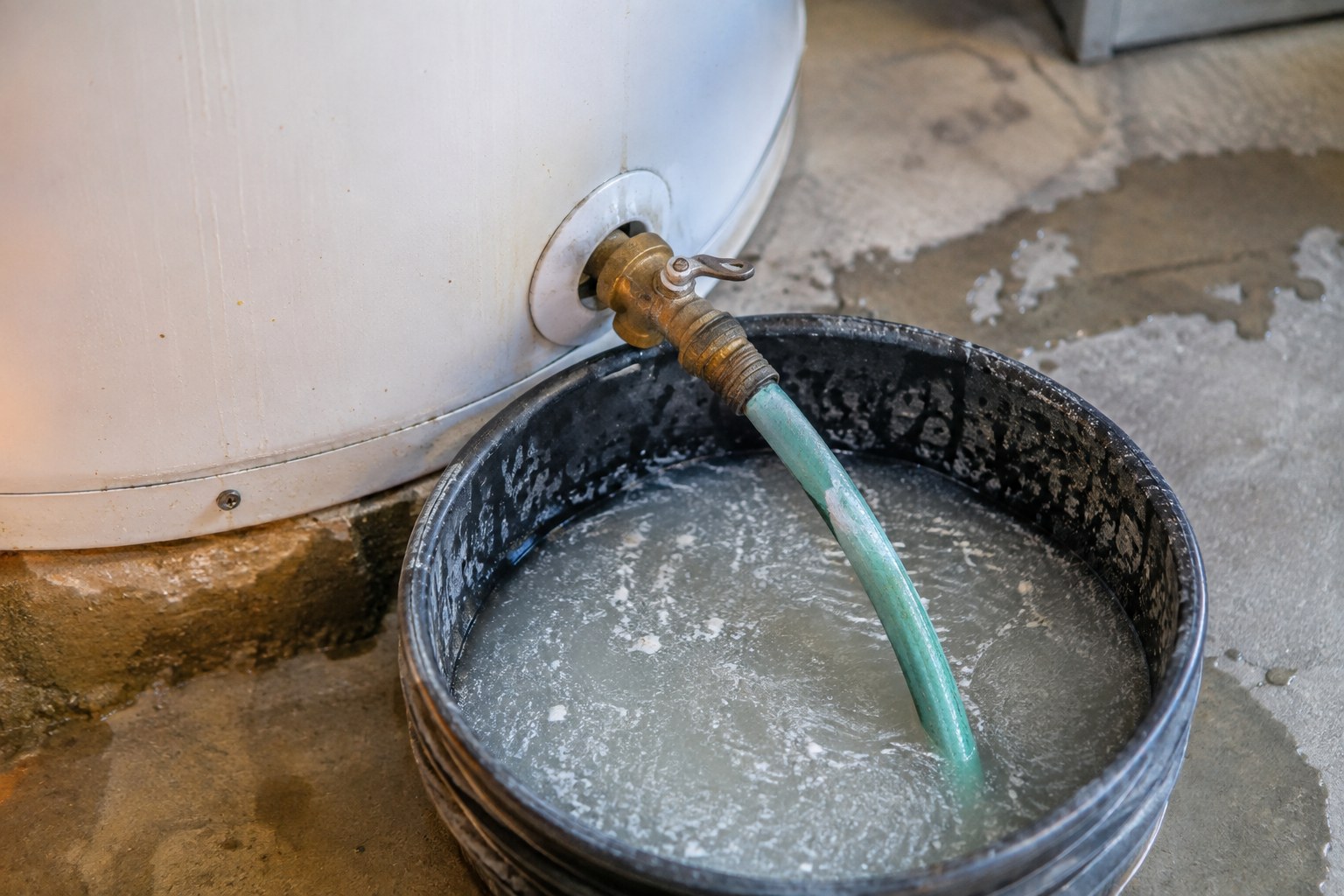 Garden hose draining cloudy, sediment-filled water from a water heater into a bucket